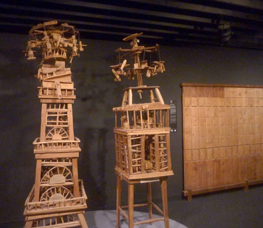 Radsport, Hitze und Erbauung 13 Zwei hohe, detailreiche Holzkonstruktionen von Émile Ratier in einem dunklen Ausstellungsraum.