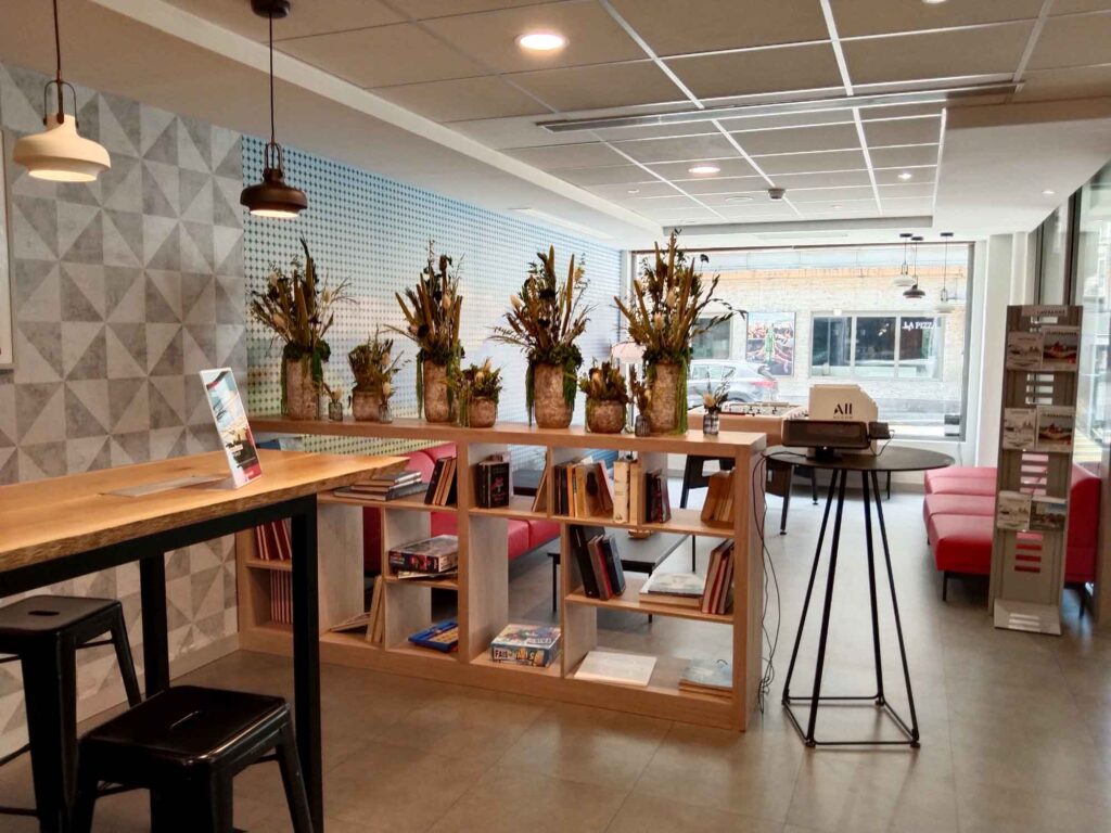 Moderner Aufenthaltsbereich im ibis Lausanne Centre mit Sitzgelegenheiten, Bücherregal, Tischen und Blumenarrangements