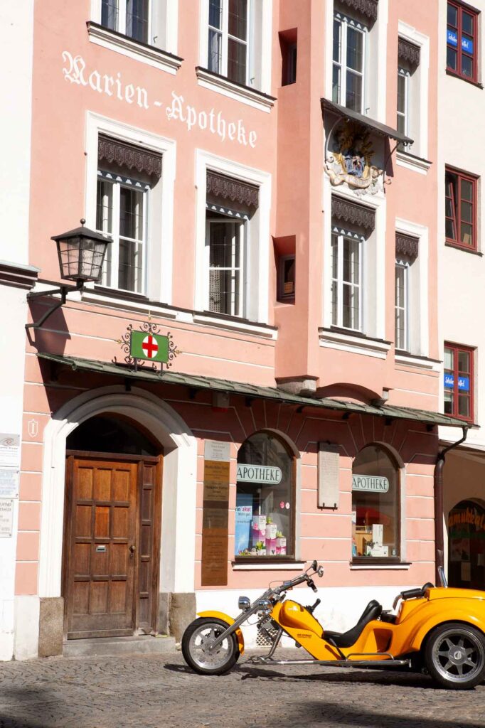 Wasserburg am Inn: Bayerische Bilderbuchstadt in der Innschleife 7 Rosafarbene historische Fassade der Marien-Apotheke in Wasserburg am Inn mit Zunftzeichen und einem gelben Trike davor.