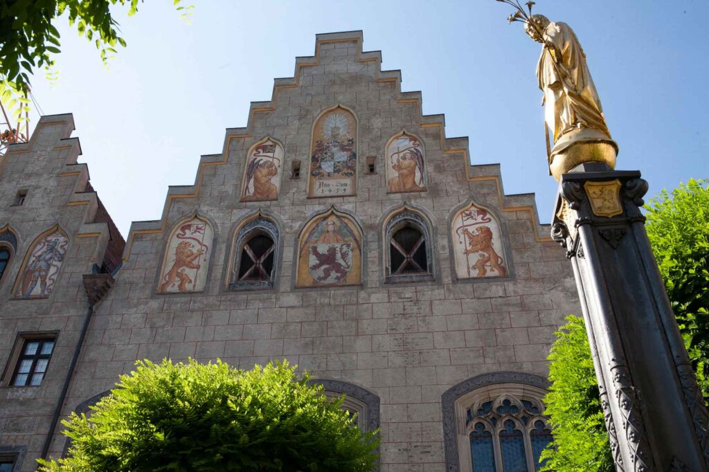 Wasserburg am Inn: Bayerische Bilderbuchstadt in der Innschleife 5 Die bemalte Treppengiebelfassade des Rathauses in Wasserburg am Inn hinter einer vergoldeten Statuensäule unter blauem Himmel.
