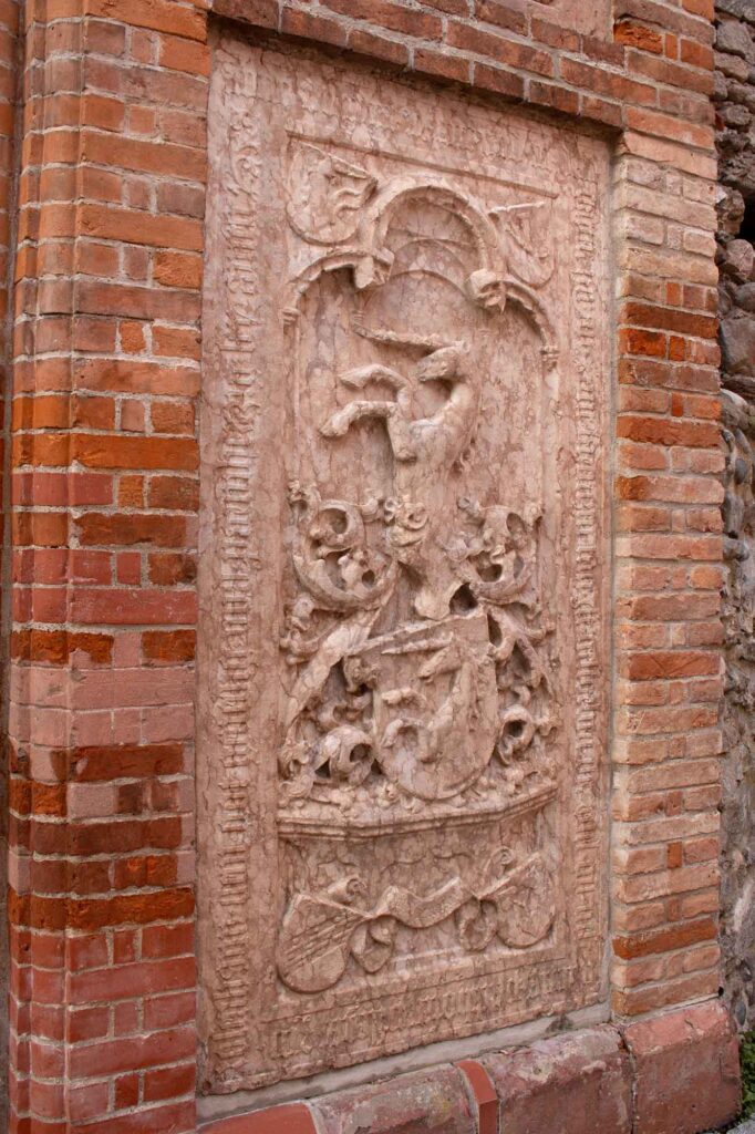 Wasserburg am Inn: Bayerische Bilderbuchstadt in der Innschleife 15 Ein historisches Epitaph aus rotem Marmor oder Stein mit einem Relief, das in die Ziegelwand am Portal des Alten Friedhofs in Wasserburg am Inn in Oberbayern eingelassen ist.