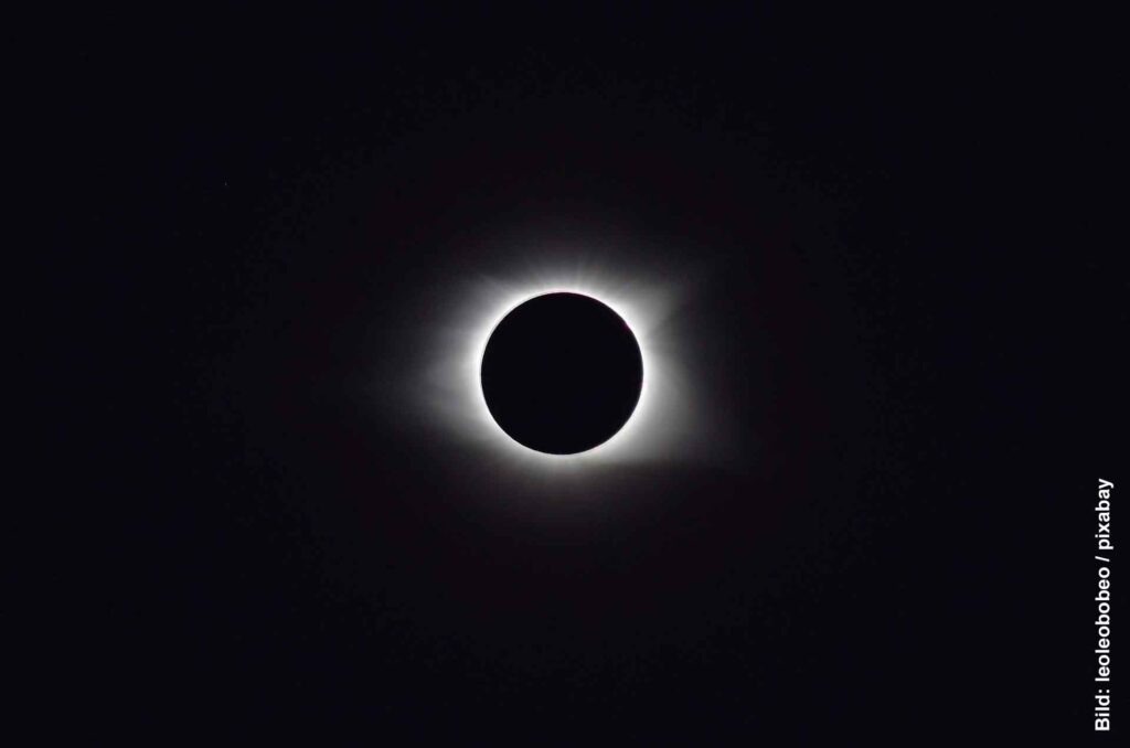 Totale Sonnenfinsternis vor dunklem Himmel mit leuchtender Korona rund um die schwarze Mondscheibe
