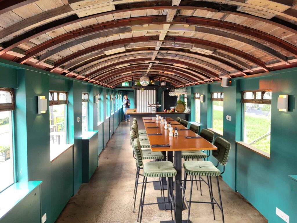 Tilburg: Wo Industriekultur auf Design und neue Ideen trifft 11 Innenraum eines historischen Eisenbahnwagens der Eetbar De Wagon mit langem Tisch und grünen Stühlen.