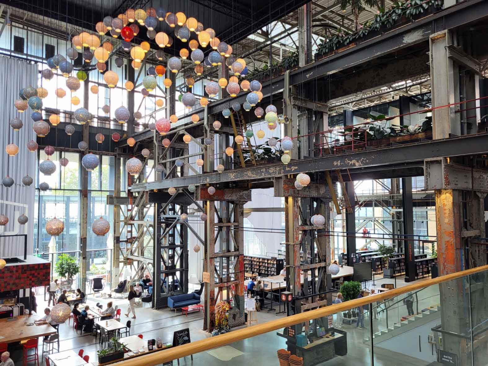 Tilburg: Wo Industriekultur auf Design und neue Ideen trifft 1 Großer Innenraum der LocHal mit alten Stahlträgern, Arbeitsplätzen und zahlreichen kugelförmigen Leuchten.
