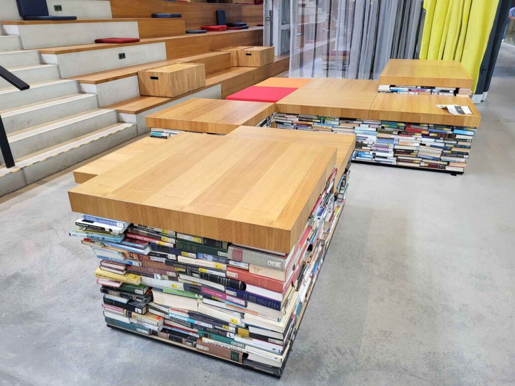 Tilburg: Wo Industriekultur auf Design und neue Ideen trifft 13 Tische und Sitzmöbel in der LocHal mit Sockeln aus dicht gestapelten Büchern und dicken Holzplatten.