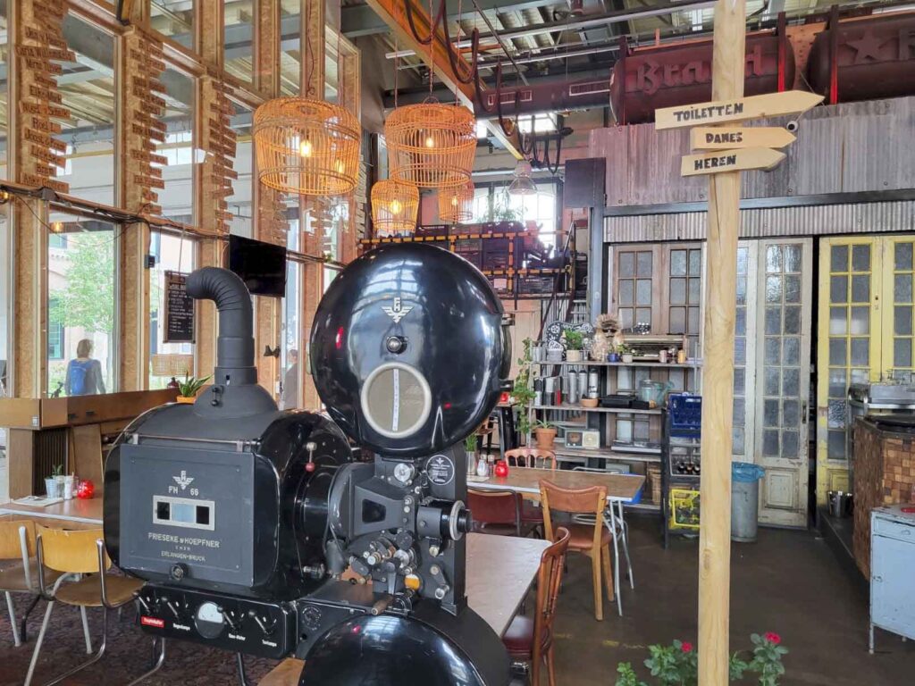 Tilburg: Wo Industriekultur auf Design und neue Ideen trifft 35 Großer historischer schwarzer Filmprojektor in einem gastronomisch genutzten Innenraum in Tilburg.