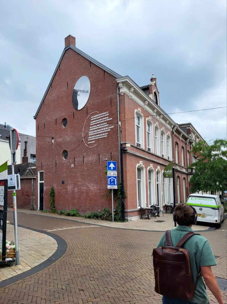 Tilburg: Wo Industriekultur auf Design und neue Ideen trifft 7 Backsteinfassade mit der Aufschrift „De Spiegelde Stad“ und einem großen runden Wandelement in Tilburg.
