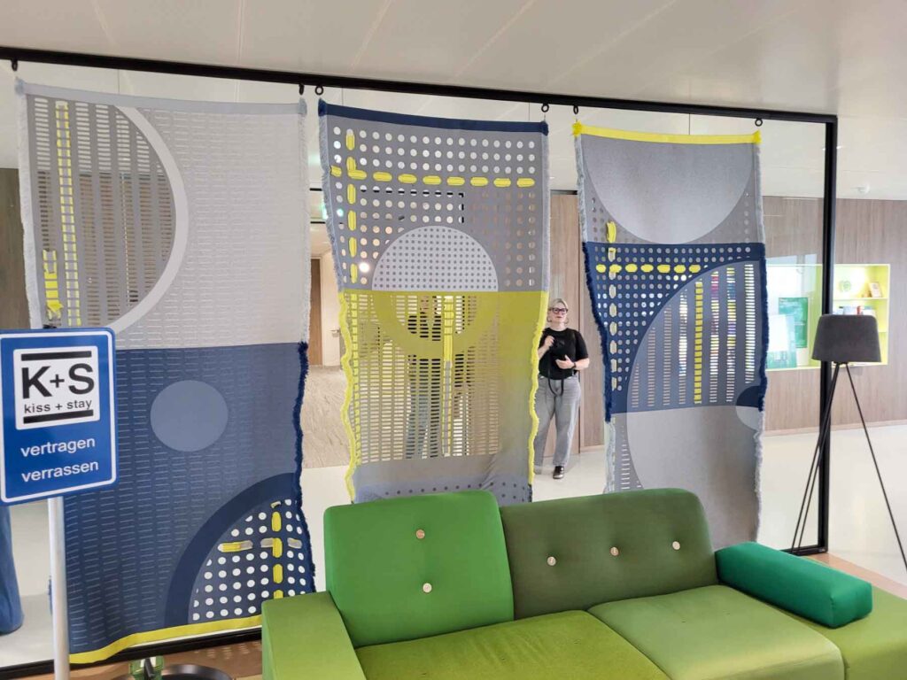 Tilburg: Wo Industriekultur auf Design und neue Ideen trifft 31 Drei großformatige textile Bahnen in Grau, Blau und Gelb hinter einem grünen Sofa im Rathaus von Tilburg.