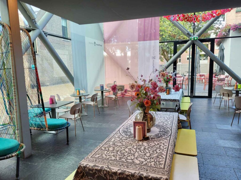 Tilburg: Wo Industriekultur auf Design und neue Ideen trifft 32 Moderner Cafébereich im TextielMuseum Tilburg mit langen Tischen, Blumen und farbigen Sitzmöbeln.