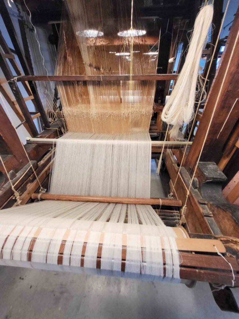 Tilburg: Wo Industriekultur auf Design und neue Ideen trifft 23 Historischer hölzerner Webstuhl mit eingespannten weißen Kettfäden im TextielMuseum Tilburg.