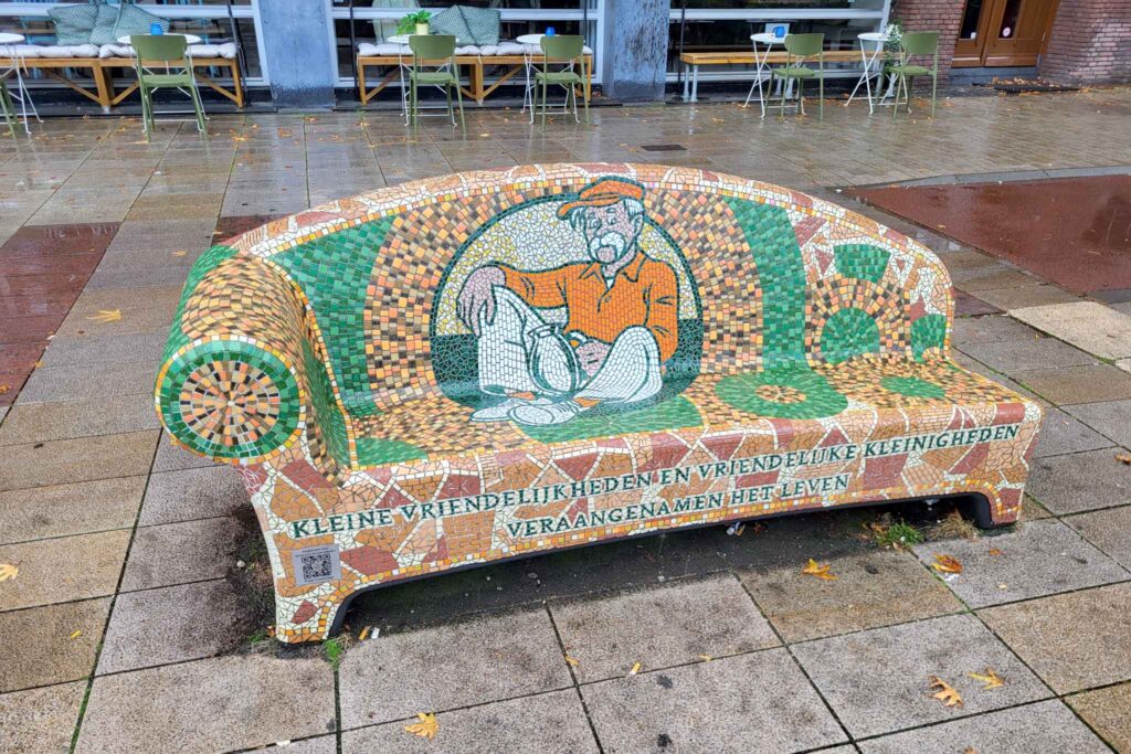 Tilburg: Wo Industriekultur auf Design und neue Ideen trifft 38 Farbenfrohe Mosaikbank mit einer sitzenden Figur in orangefarbener Kleidung im Zentrum von Tilburg.