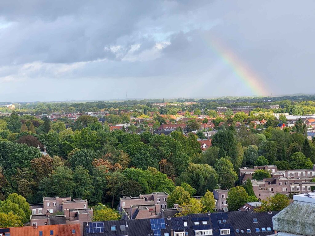 Eindhoven: Vom Philips-Erbe zur Zukunftsstadt 7 Panoramablick über grüne Stadtviertel Eindhovens mit Regenbogen unter dunklen Wolken.