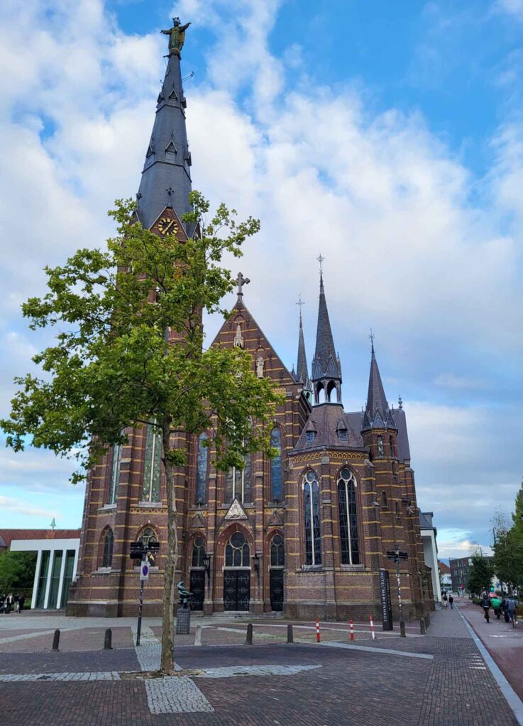 Eindhoven: Vom Philips-Erbe zur Zukunftsstadt 14 Neugotische Paterskerk in Eindhoven mit hohem Turm, Herz-Jesu-Figur und blau bewölktem Himmel.
