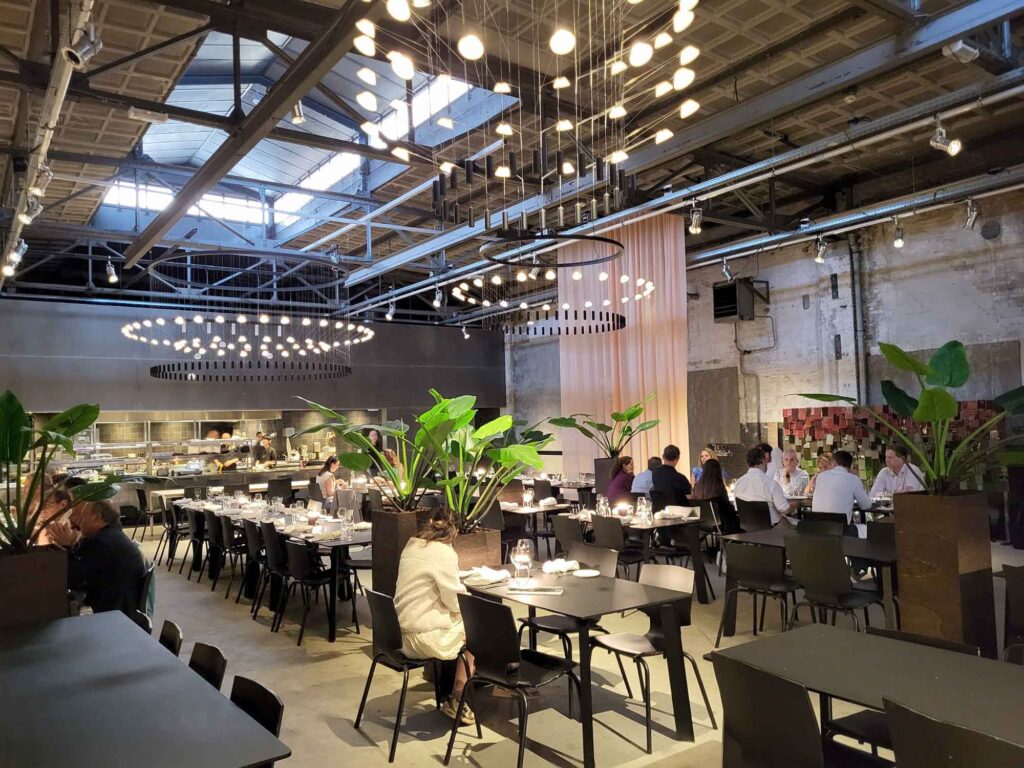 Eindhoven: Vom Philips-Erbe zur Zukunftsstadt 18 Abendlicher Gastraum des Restaurants Kazerne mit schwarzen Tischen, Pflanzen, Designleuchten und offener Küche.
