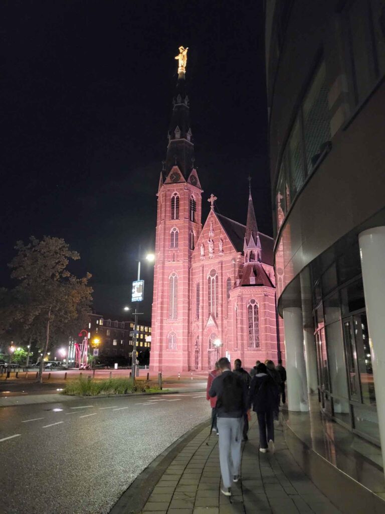 Eindhoven: Vom Philips-Erbe zur Zukunftsstadt 5 Bei Nacht rötlich beleuchtete neogotische Paterskerk in Eindhoven mit hohem Kirchturm.