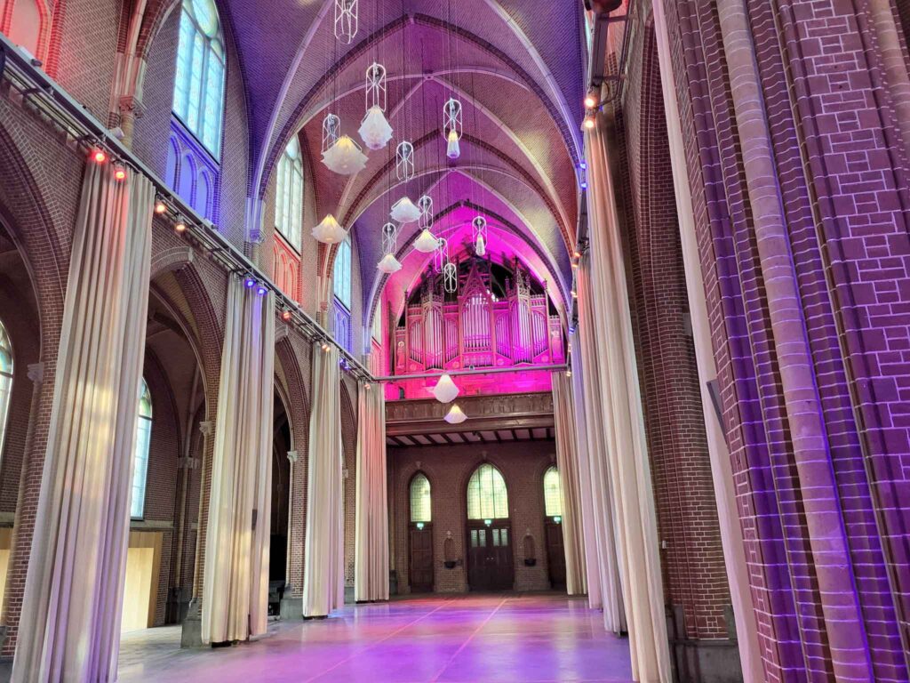 Eindhoven: Vom Philips-Erbe zur Zukunftsstadt 27 Innenraum der Paterskerk mit violetter und roter Beleuchtung, hohen Vorhängen, Gewölben und Orgel.