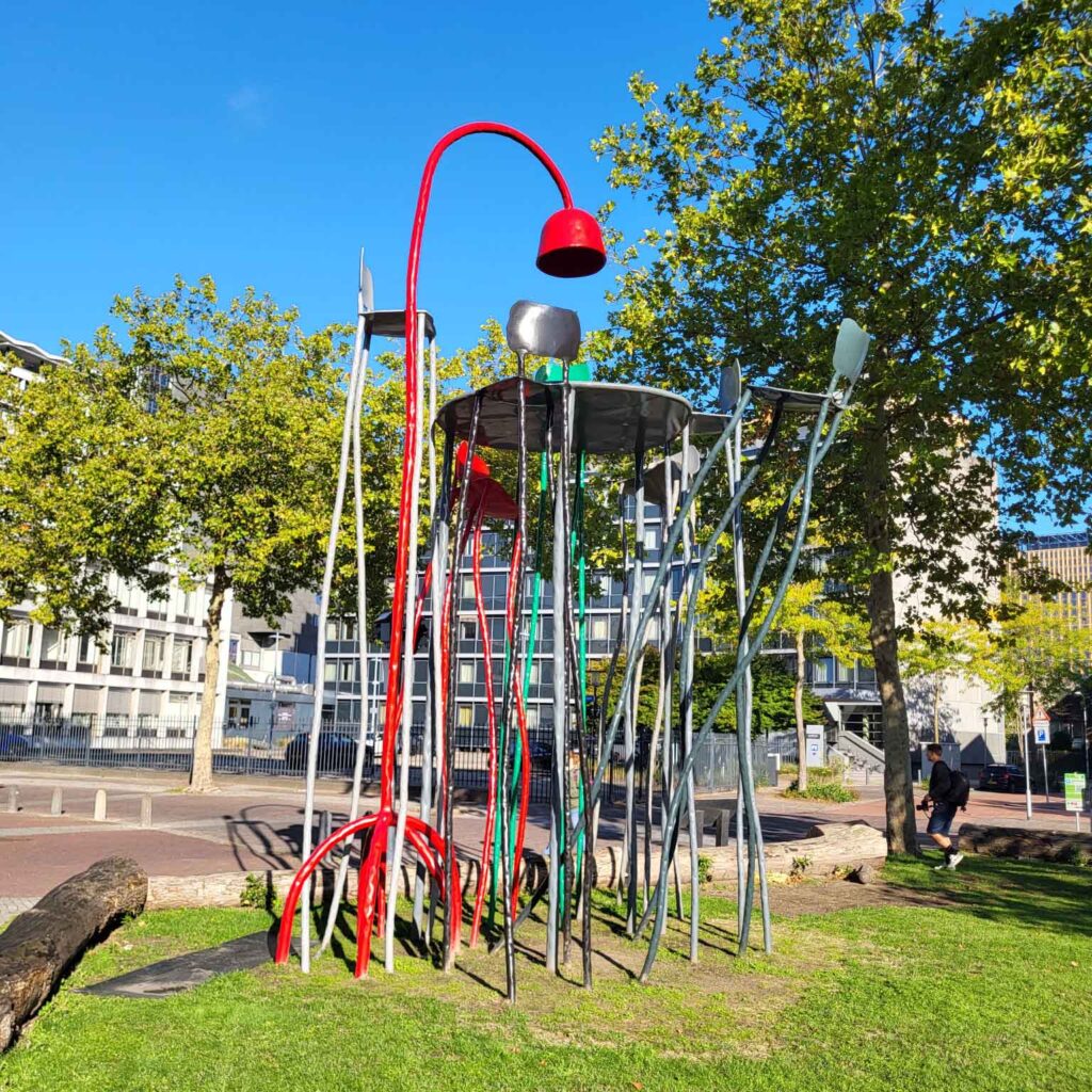 Eindhoven: Vom Philips-Erbe zur Zukunftsstadt 16 Skulptur aus langen farbigen Metallformen, Stühlen und einer roten bogenförmigen Leuchte auf einer Grünfläche in Eindhoven.