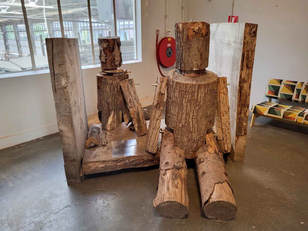Eindhoven: Vom Philips-Erbe zur Zukunftsstadt 37 Zwei sitzende menschenähnliche Figuren aus groben Baumstämmen und Holzstücken in einem Ausstellungsraum.