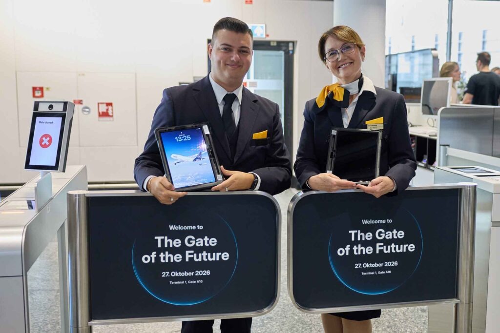 Gate of the Future: Lufthansa und Fraport testen das Boarding der Zukunft 3 Zwei Lufthansa-Mitarbeitende in Uniform präsentieren Tablets hinter den Anzeigen des „Gate of the Future“ in Frankfurt.